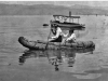 " negative of two people paddling a tule boat.